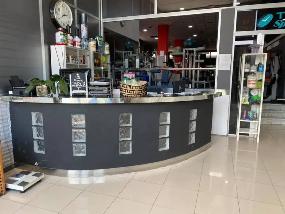 Mostrador de recepción con suplementos y reloj, y la sala de máquinas al fondo