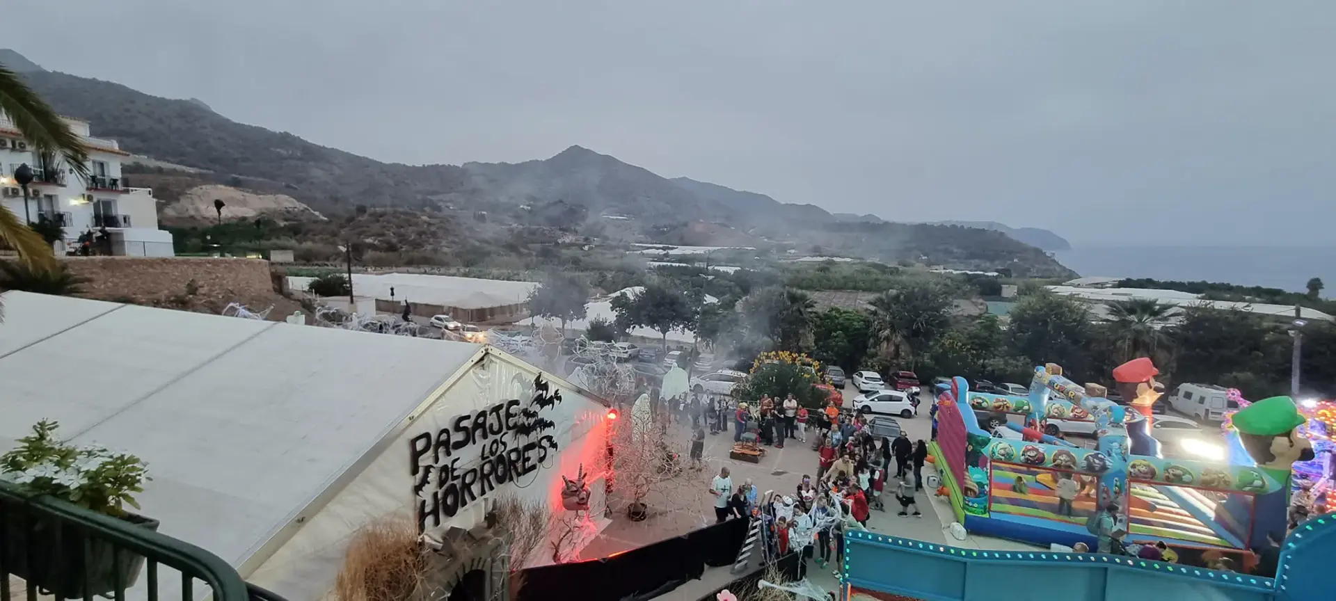 Carpa del Pasaje de los Horrores e hinchables en Maro al anochecer, con la sierra y el mar