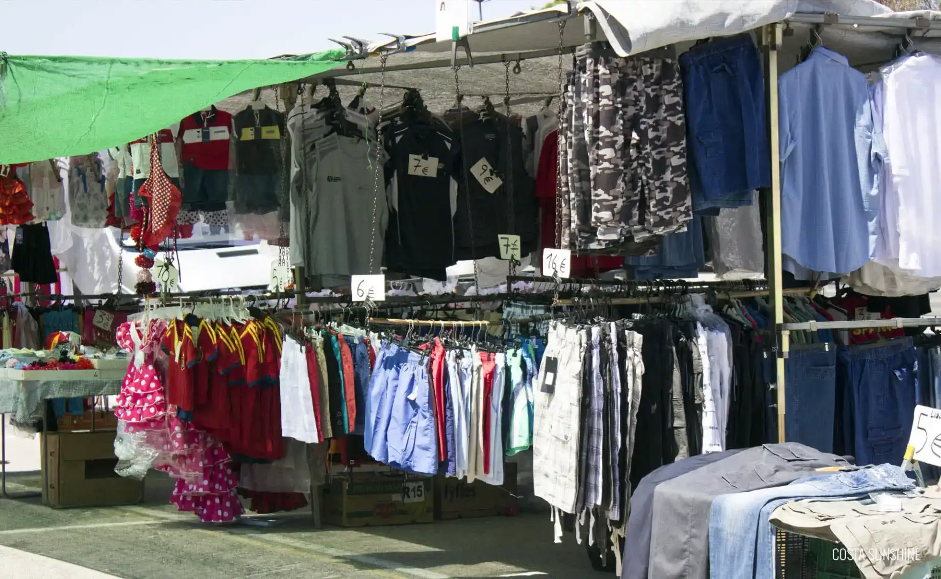 Puesto de ropa con camisetas, pantalones y vestidos colgados en perchas en el mercadillo