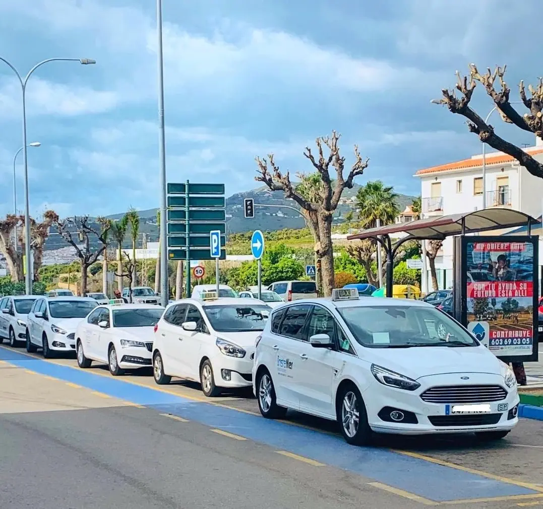 Fila de taxis en una parada señalizada en azul, con la sierra al fondo