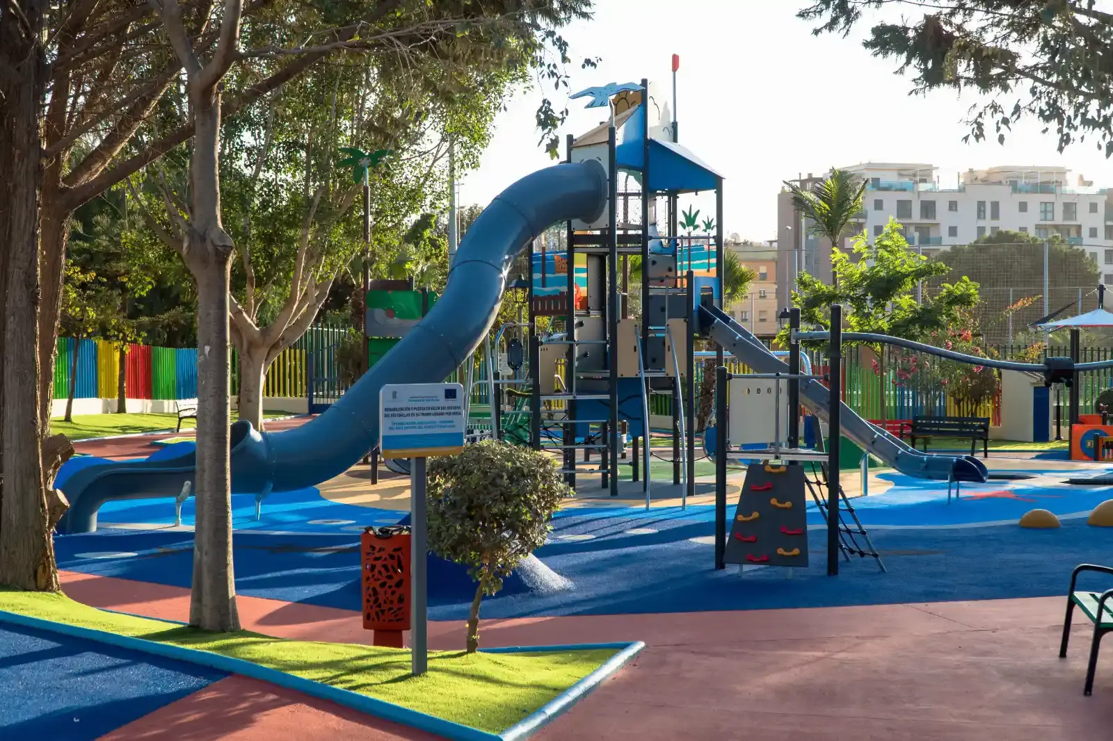 Torre de juegos con tobogán de tubo azul entre árboles en el parque infantil
