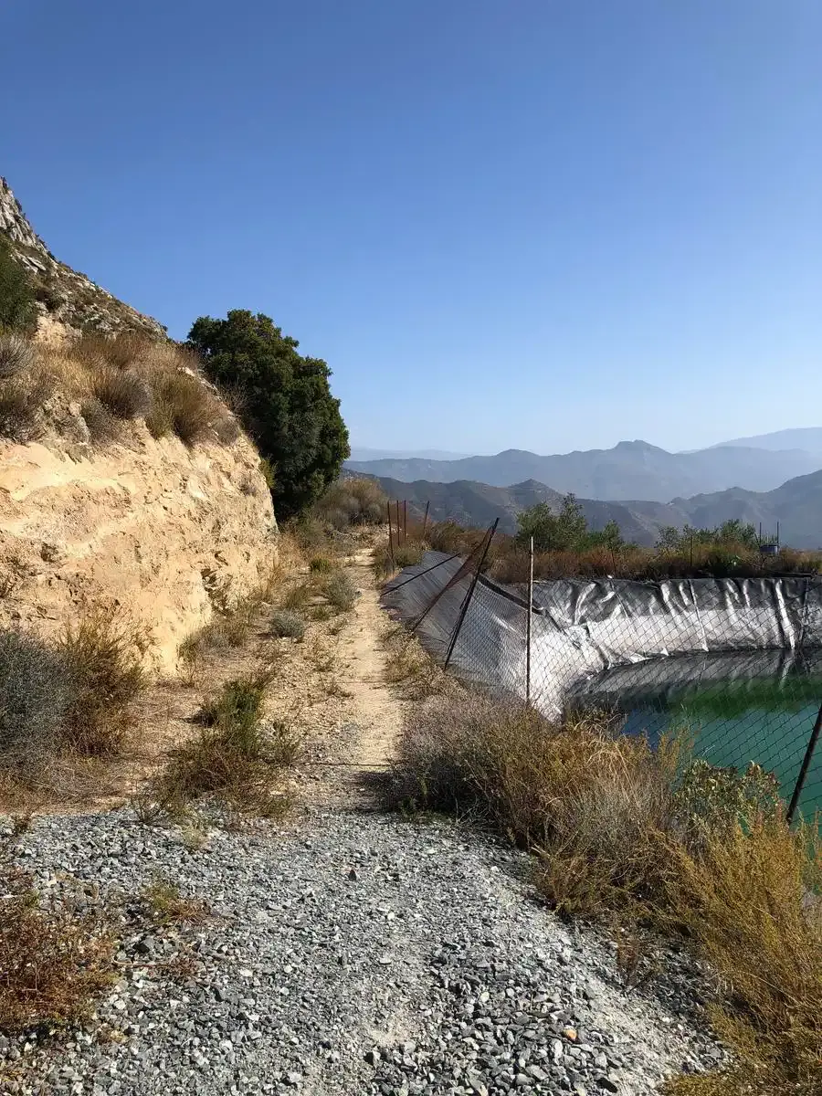 Pista de grava junto a una balsa de riego, con la ladera rocosa a un lado