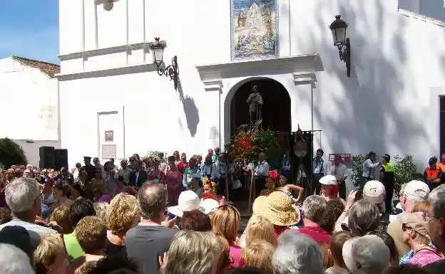 Público reunido ante la iglesia blanca mientras sale la imagen de San Isidro con flores