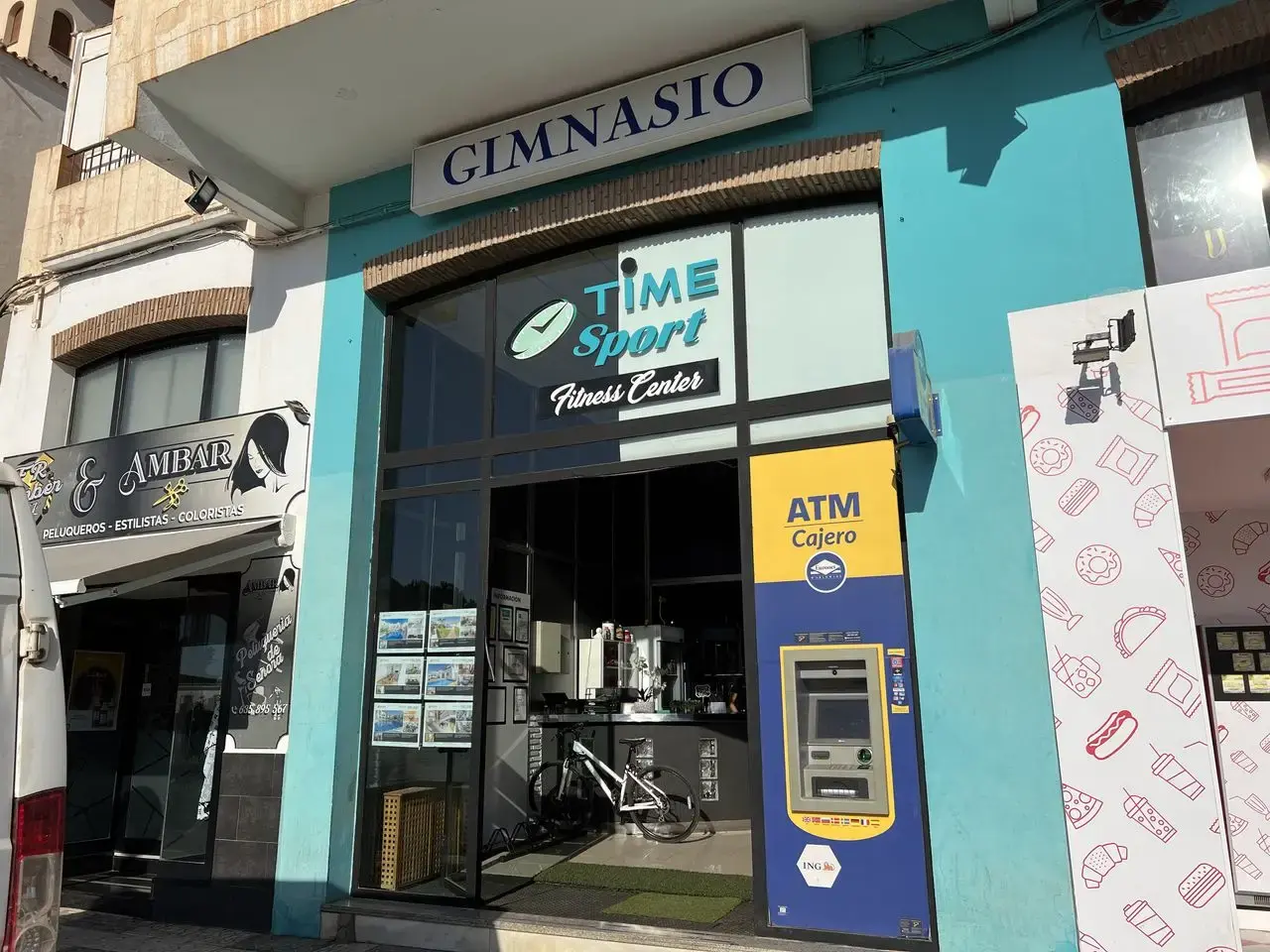 Fachada del gimnasio Time Sport Fitness Center con rótulo azul y un cajero automático al lado