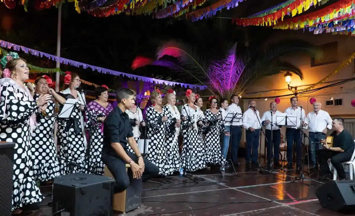 Coro con trajes de lunares actuando de noche en la Veladilla de San Miguel, bajo guirnaldas