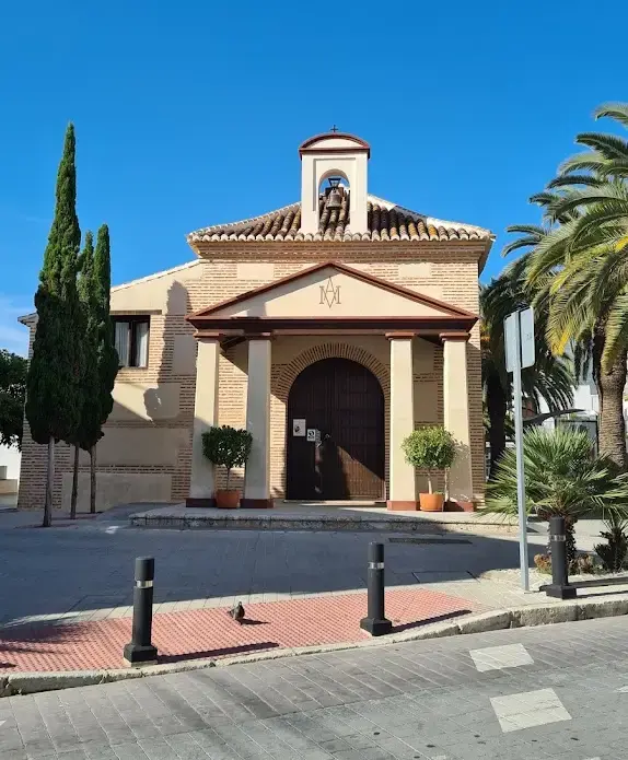 Fachada de ladrillo de la ermita con espadaña, campana y pórtico frente a la calle