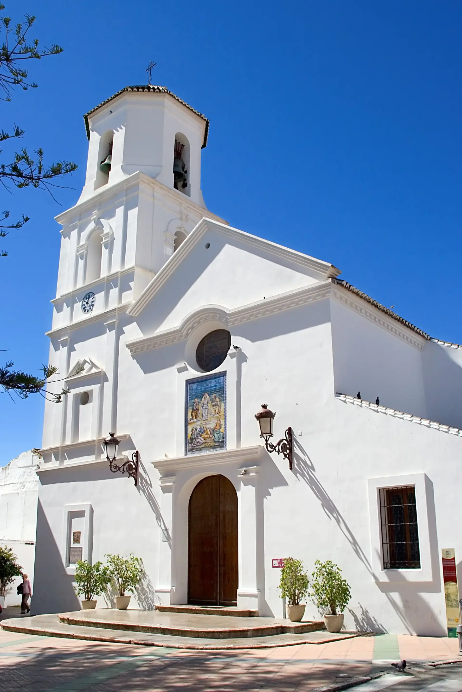 Campanario y fachada encalada de El Salvador con mosaico de azulejos sobre la puerta