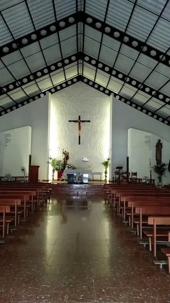 Interior de la iglesia con bancos de madera, techo a dos aguas y un gran crucifijo en el altar