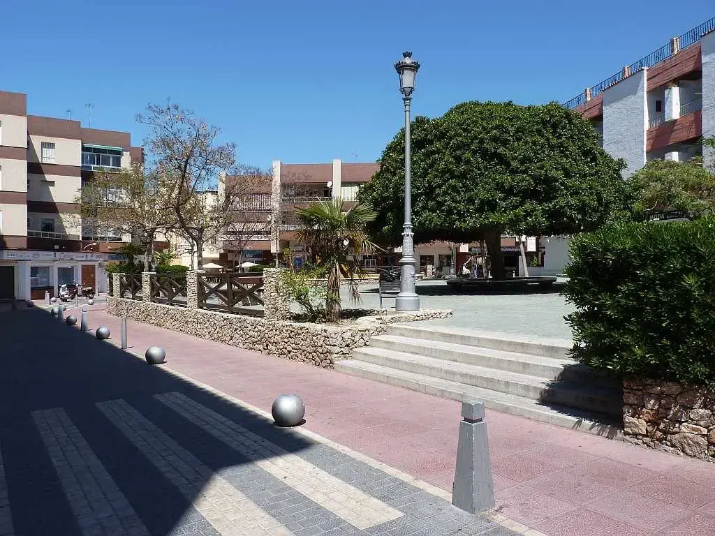 Escalones de acceso a la plaza peatonal, con farola, árbol frondoso y edificios de apartamentos