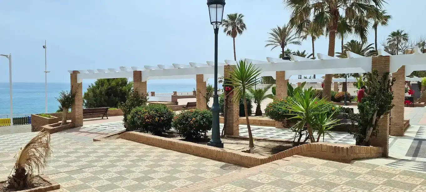 Pérgola blanca con jardineras y farola, frente al mar
