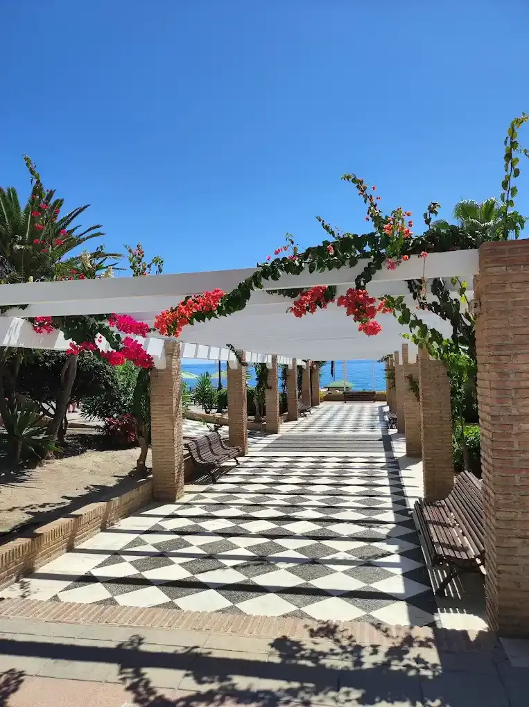 Pérgola con buganvillas sobre un pasillo de baldosas blancas y negras hacia el mar