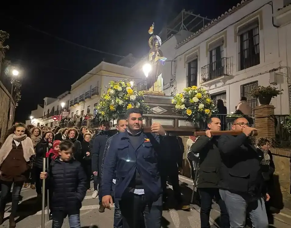 Portadores llevando a hombros la imagen del santo por una calle de Maro, seguidos por vecinos