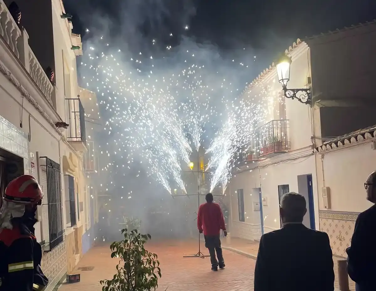 Fuente de chispas de fuegos artificiales en una calle blanca durante la fiesta, con un bombero vigilando