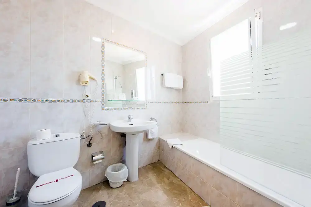 Baño con bañera, lavabo de pie, espejo con cenefa de azulejos y secador