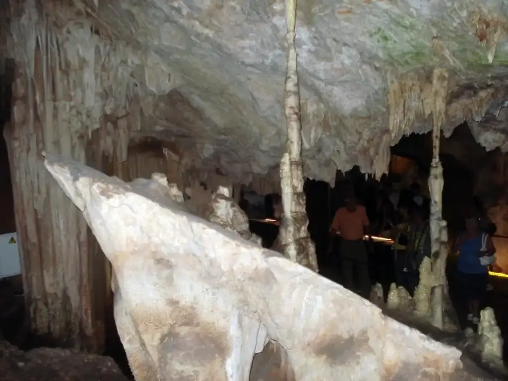 Visitantes entre columnas y formaciones calcáreas en una sala en penumbra de la cueva