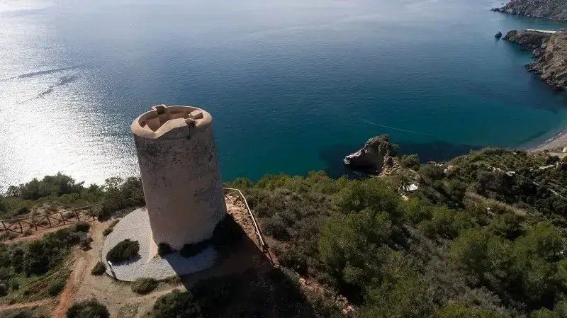 Vista aérea de la torre sobre el acantilado y una cala de aguas turquesa