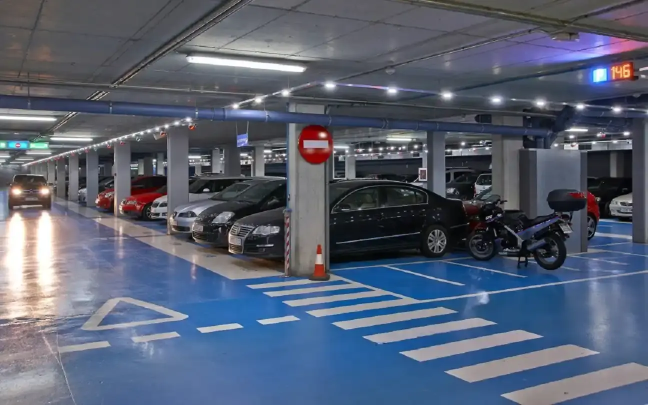 Aparcamiento subterráneo con suelo azul, coches y una moto aparcados y contador de plazas libres