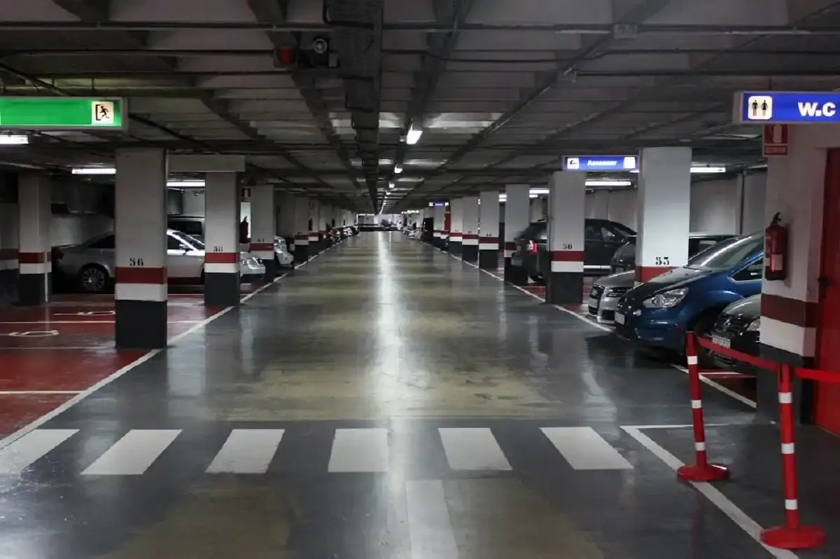 Planta del aparcamiento subterráneo con coches aparcados, columnas numeradas y señal de aseos