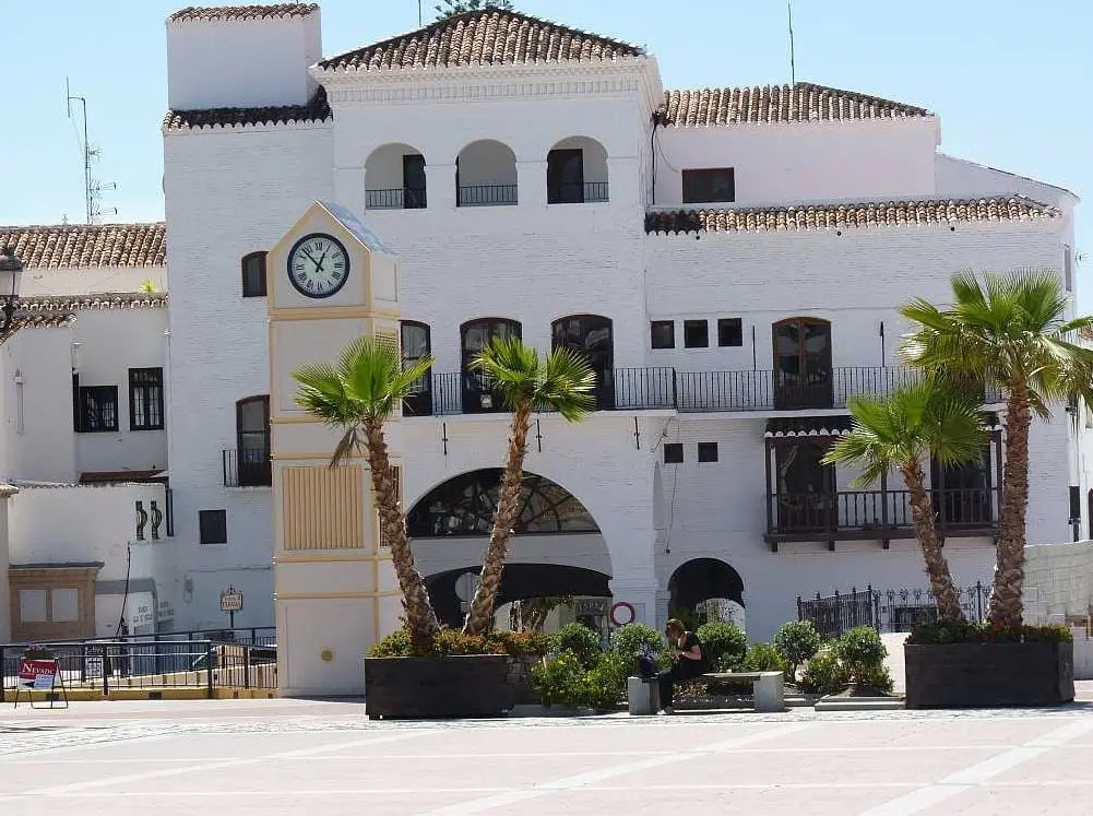 Edificio del ayuntamiento con torre del reloj y palmeras en la plaza, un día soleado