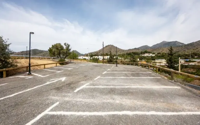 Aparcamiento asfaltado con plazas pintadas y vallas de madera, con la sierra al fondo