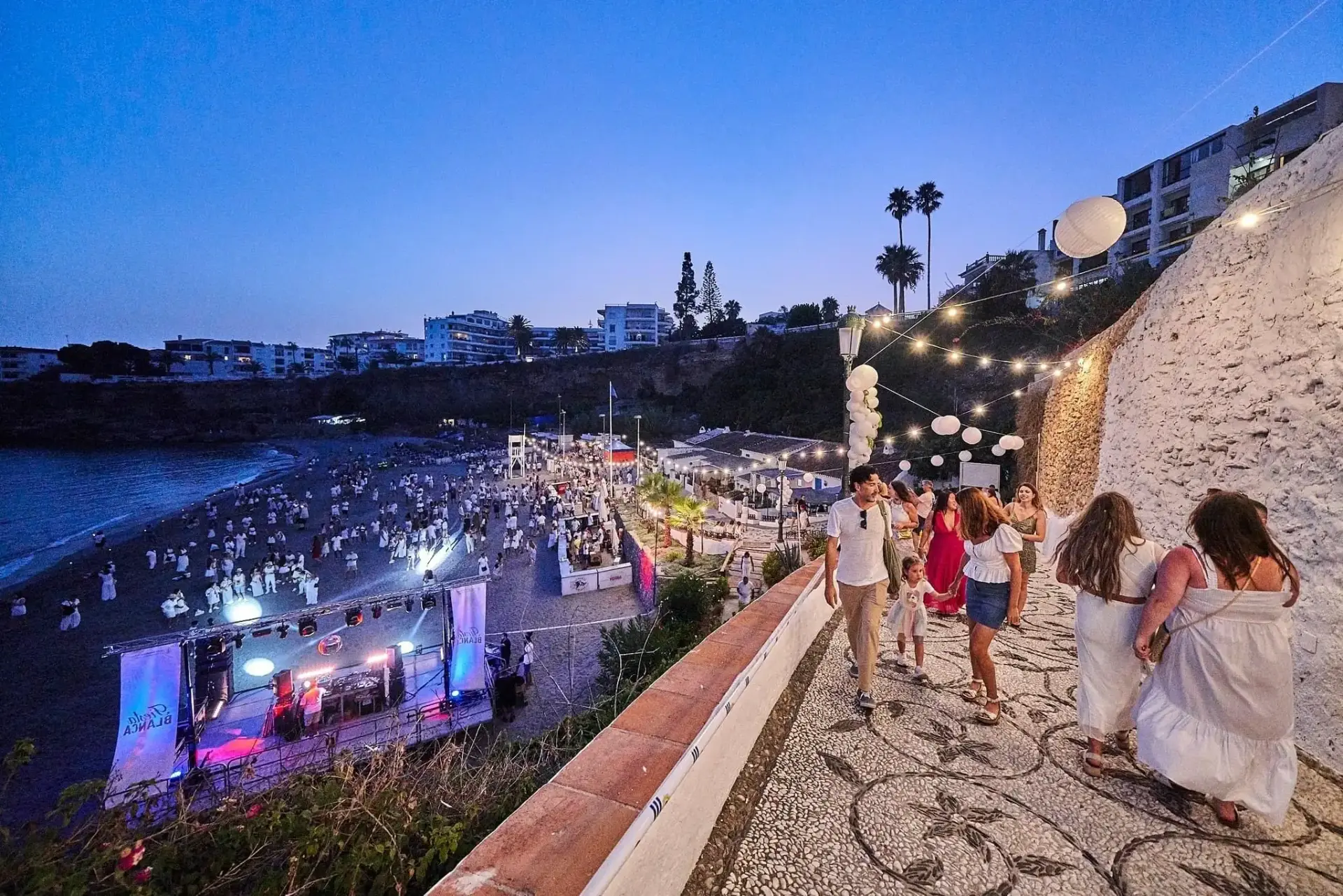 Gente de blanco bajando a la Fiesta Blanca, con el escenario y la playa llena al fondo