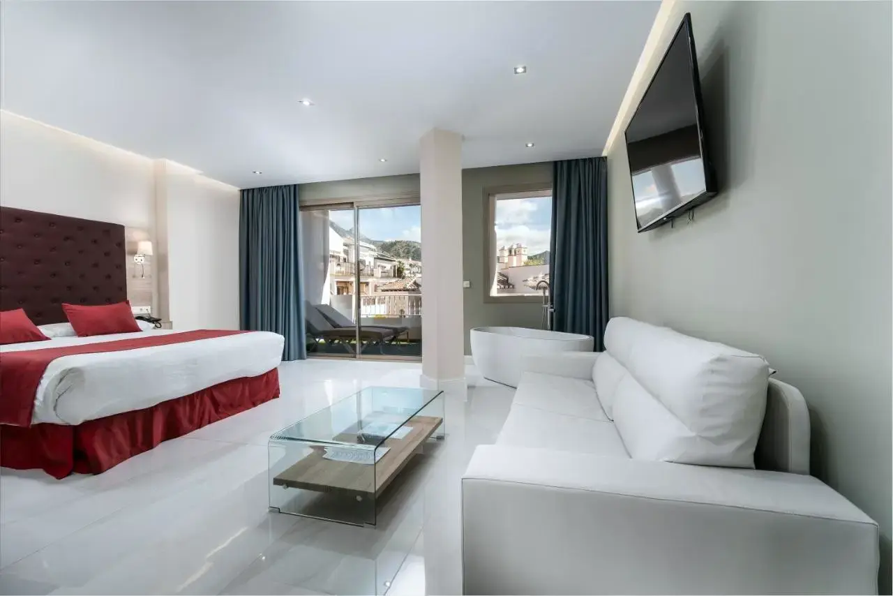 Suite con cama grande, sofá blanco, bañera exenta y terraza con tumbonas