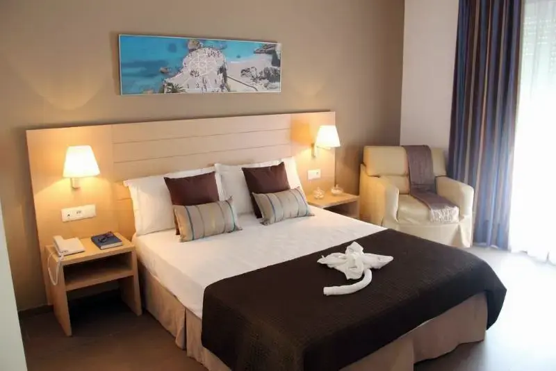 Habitación con cama de matrimonio, cojines, lámparas de pared y sillón junto a la ventana