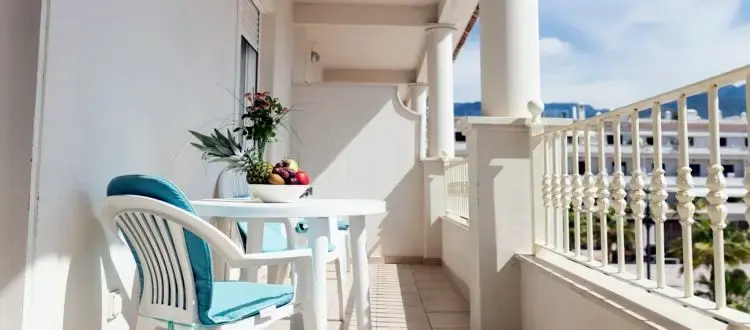Balcón con mesa blanca, frutero y sillas con cojines azules en el Hotel Mena Plaza