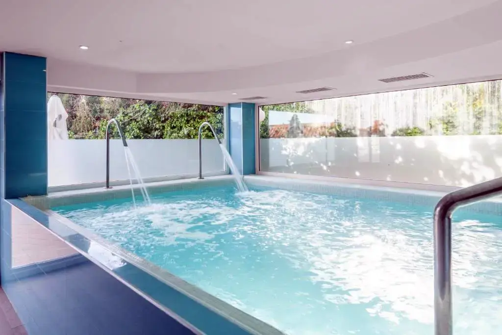 Piscina climatizada interior con chorros de agua y grandes ventanales