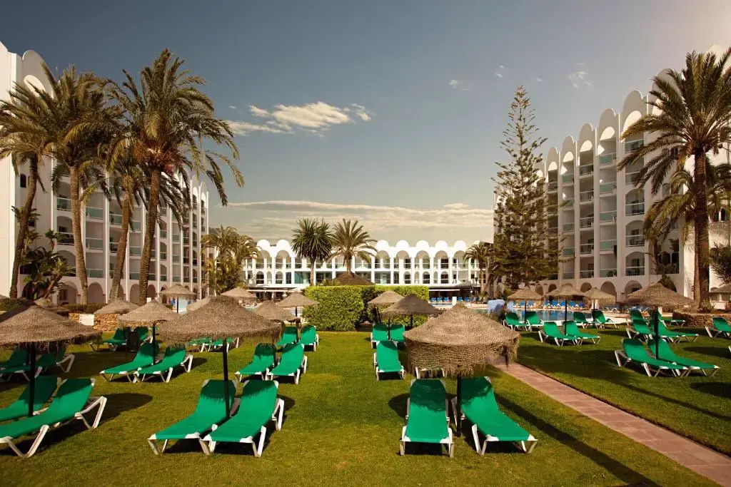Jardín con tumbonas verdes y sombrillas de brezo entre los edificios del Hotel Marinas de Nerja