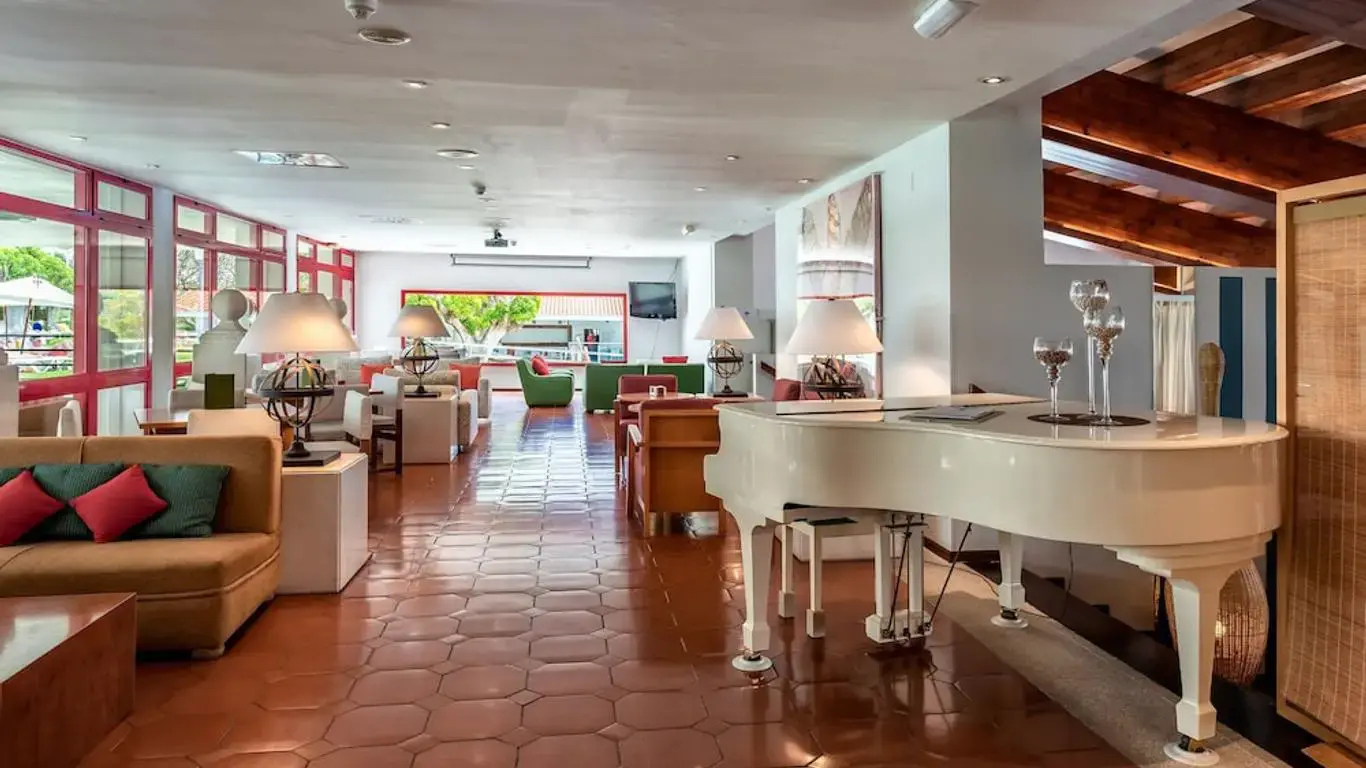 Salón con sofás, lámparas de mesa y un piano de cola blanco junto a los ventanales