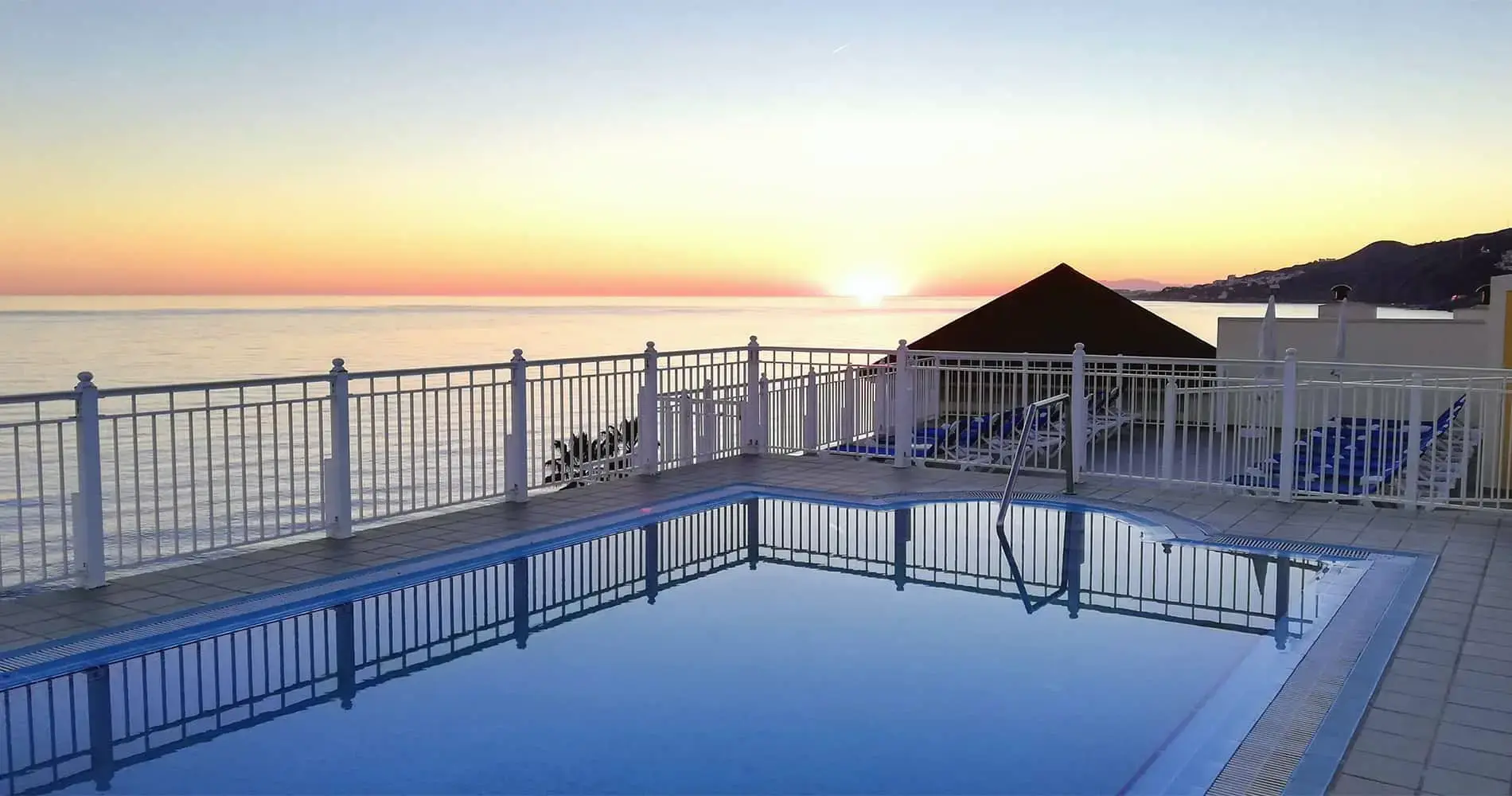 Piscina de la azotea al atardecer, con el sol poniéndose sobre el mar