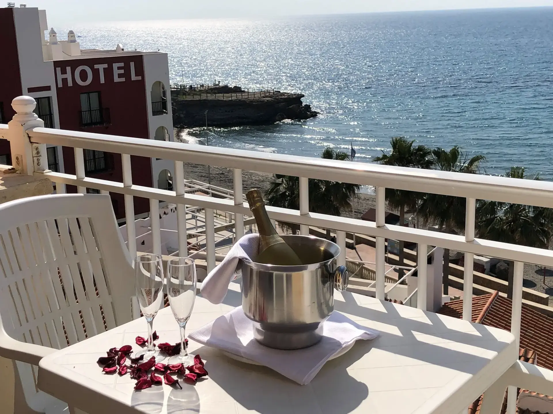 Balcón con cava en cubitera, copas y vistas al mar y a un promontorio rocoso