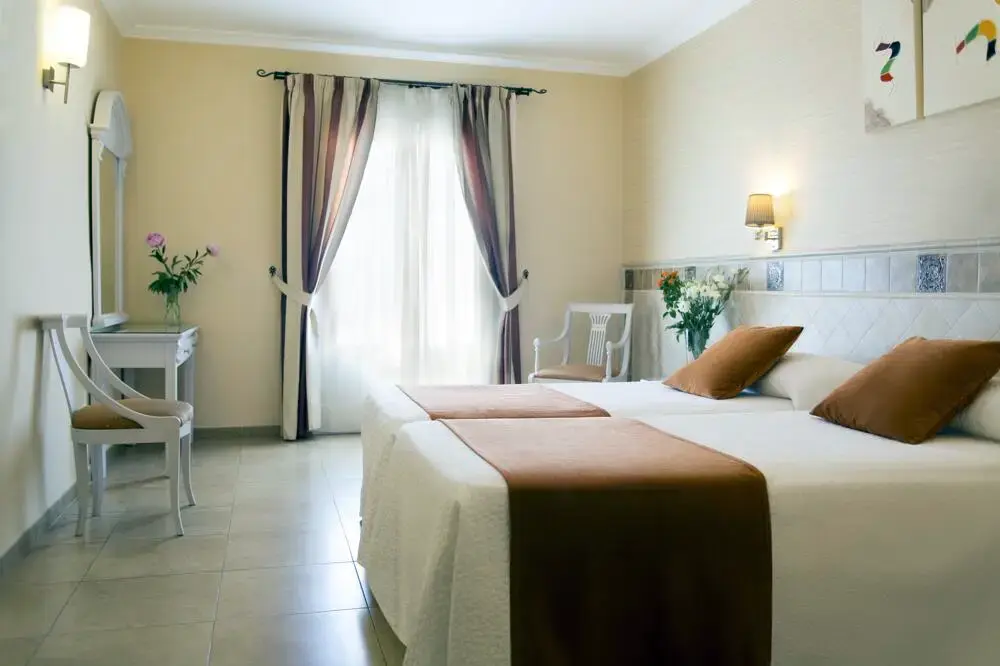 Habitación doble con dos camas, tocador blanco y ventanal con cortinas de rayas