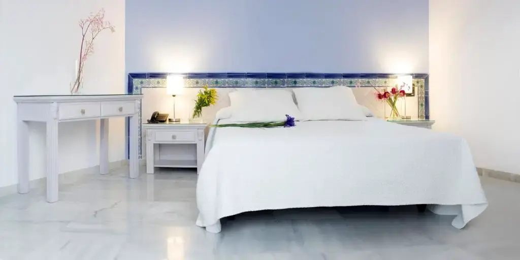 Habitación con cama de matrimonio blanca, suelo de mármol y cabecero de azulejos
