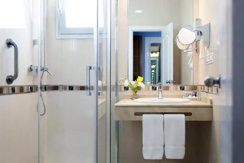 Baño con ducha de mampara, lavabo de encimera, toallas blancas y espejo de aumento