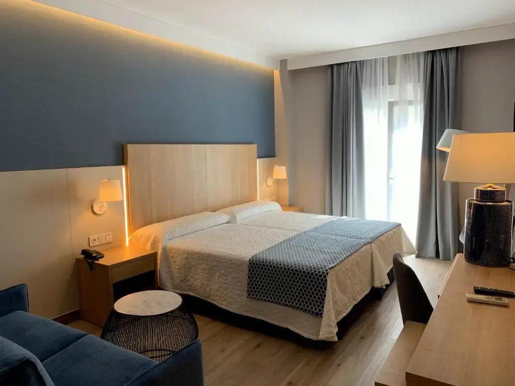 Habitación con dos camas juntas, pared azul, sofá y escritorio con lámpara