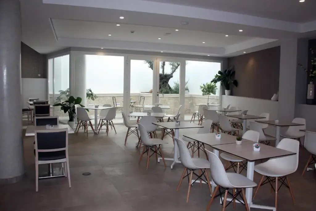 Comedor con mesas y sillas blancas y ventanales que dan a una terraza con olivo