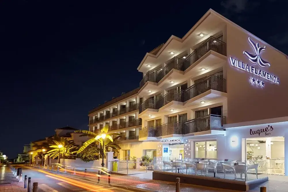 Fachada del Hotel Villa Flamenca de noche, con su letrero luminoso y la terraza del bar