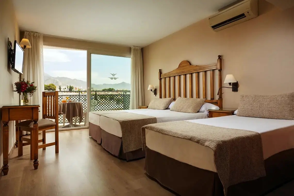 Habitación con dos camas, escritorio de madera y balcón con vistas a la sierra