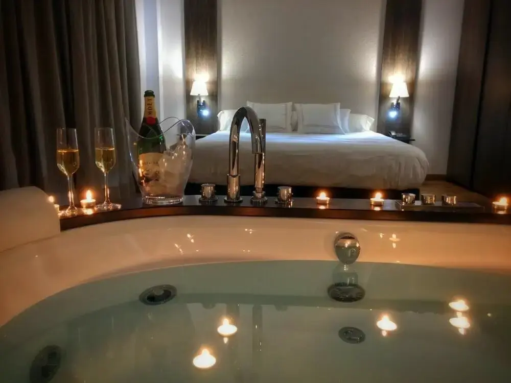 Bañera de hidromasaje con velas y cava frente a la cama de matrimonio, de noche