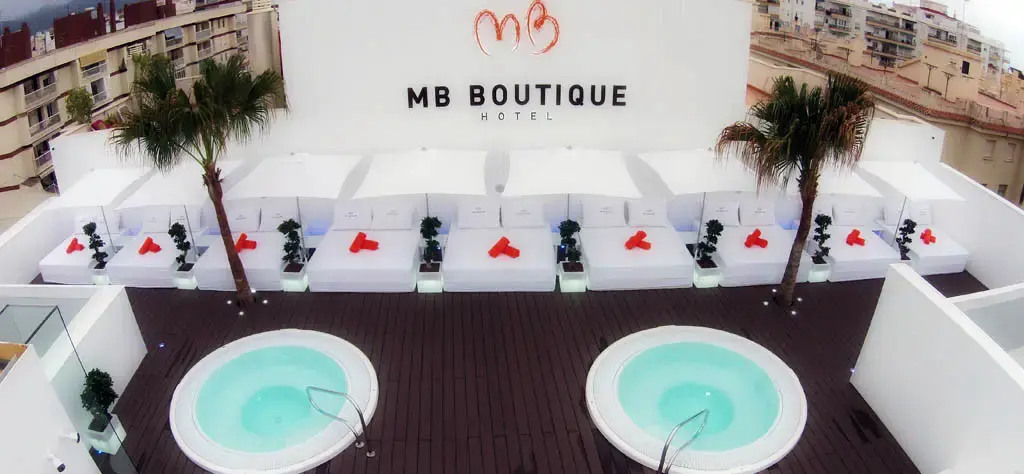 Solárium con dos jacuzzis redondos, camas blancas con cojines rojos y palmeras