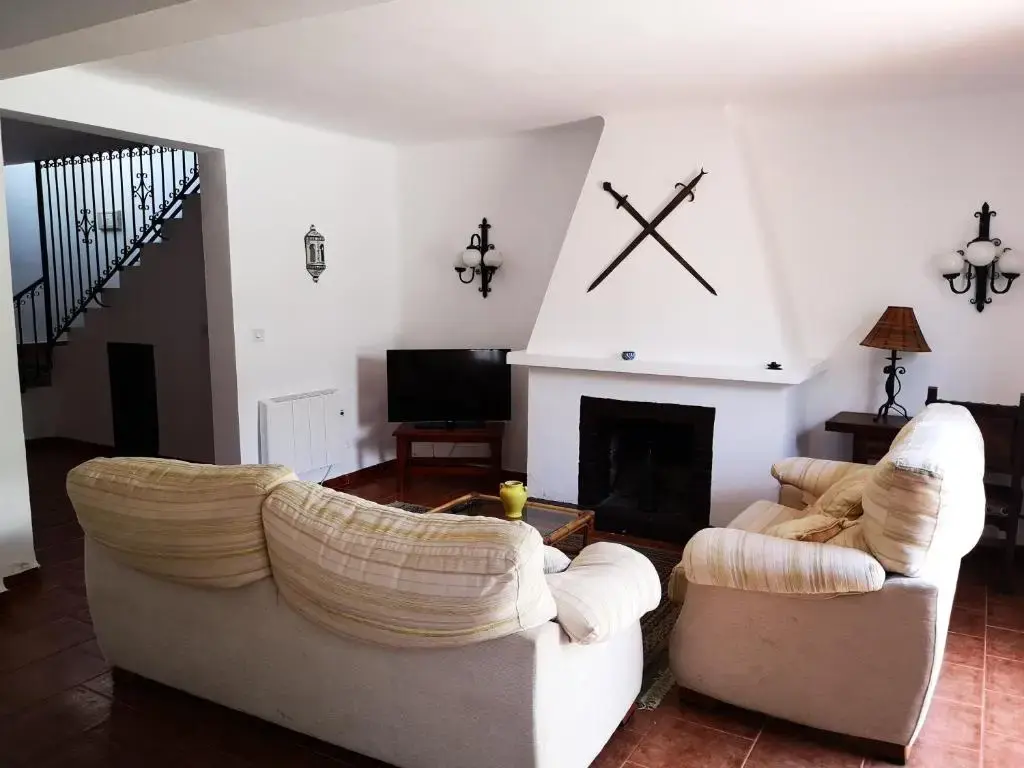 Salón con dos sofás claros, chimenea blanca con espadas cruzadas y escalera de forja