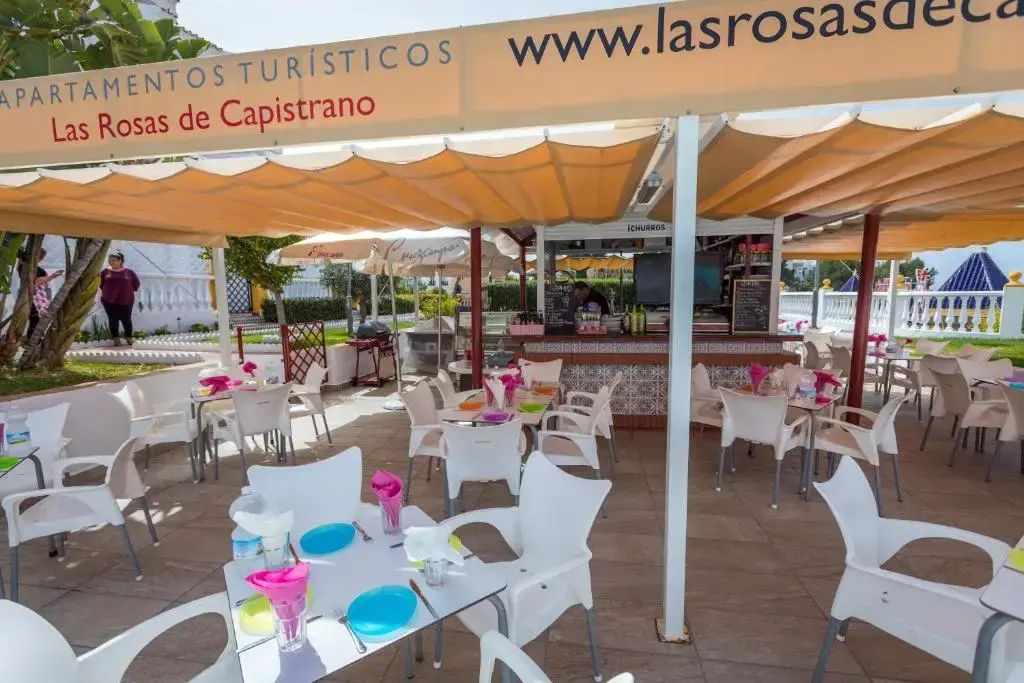 Bar-cafetería con toldos y mesas blancas en la terraza de Las Rosas de Capistrano