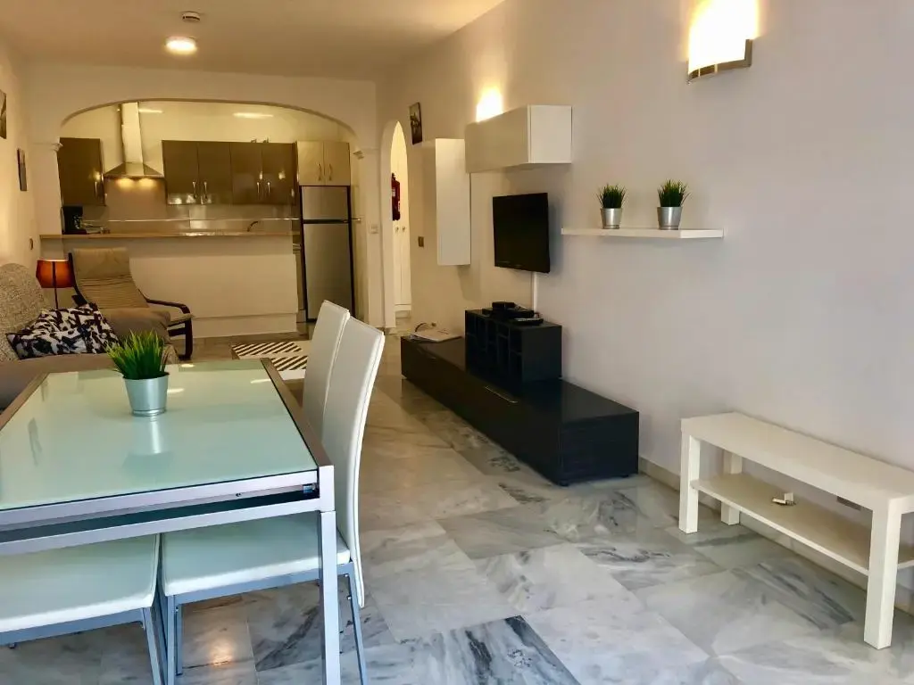 Comedor con mesa de cristal junto al salón y la cocina americana al fondo