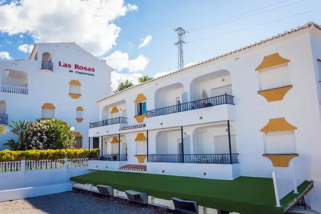 Fachada blanca con detalles amarillos y balcones de Las Rosas de Capistrano bajo el cielo azul