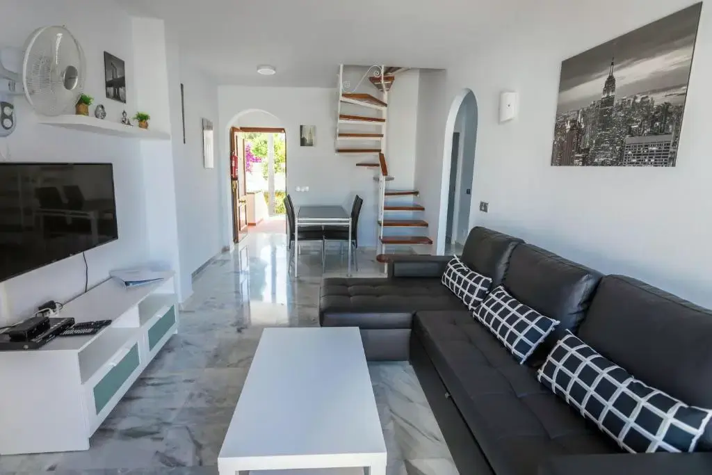 Salón con sofá negro, televisor y escalera de caracol que sube al piso superior