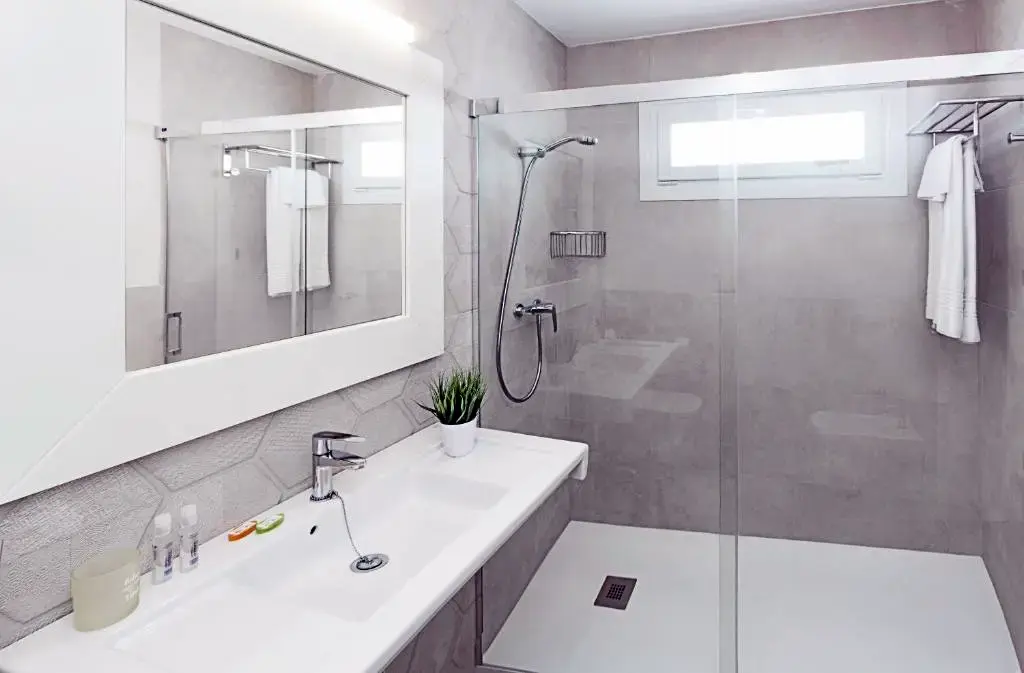 Baño con lavabo blanco, espejo grande y ducha a ras de suelo con mampara