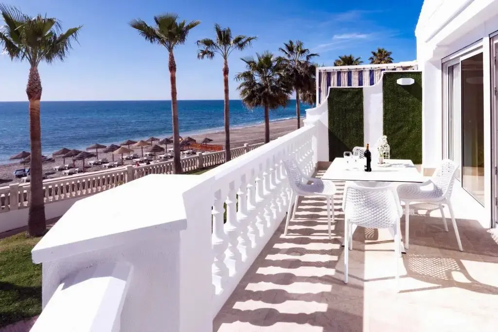 Terraza con mesa blanca y sillas sobre la playa, con palmeras y el mar delante