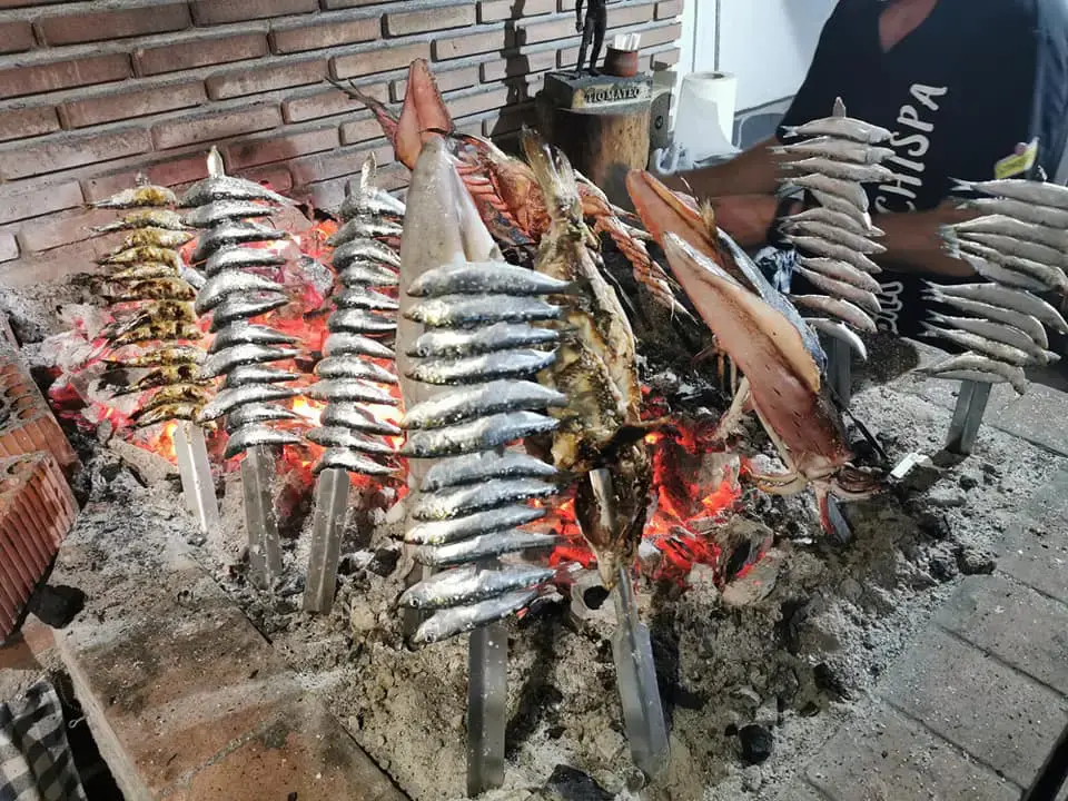 Espetos de sardinas y otros pescados asándose sobre las brasas